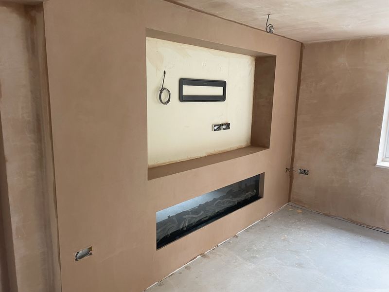 A media wall in fresh plaster with a large TV recess and a long recess for an electric fire
