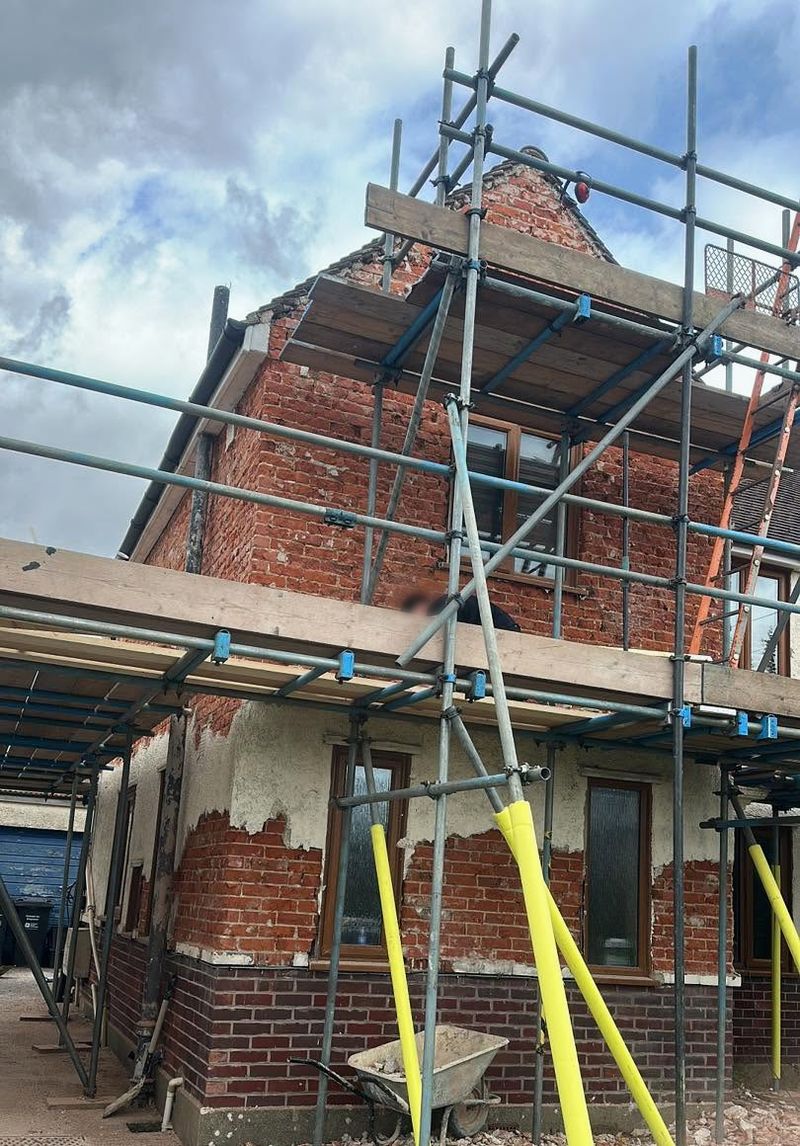 A house on scaffolding with the old render coming off and brick showing on the walls
