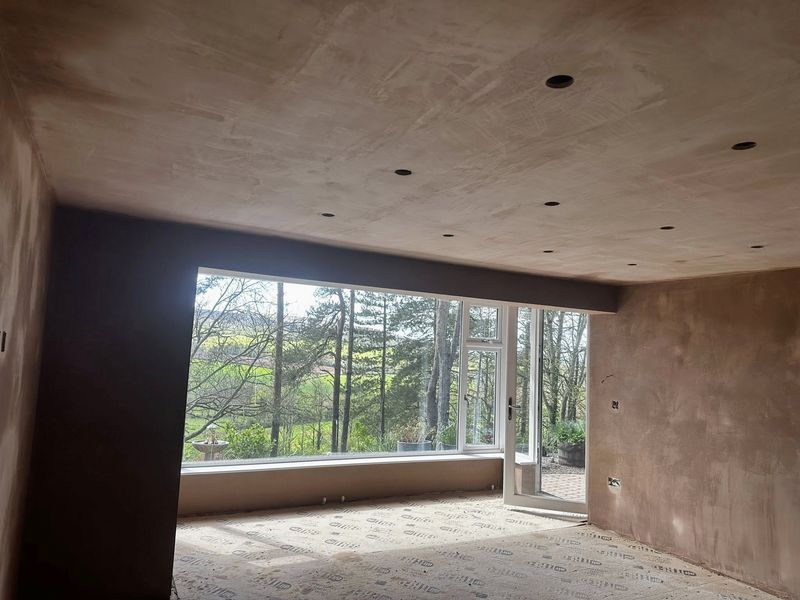 An extension freshly skimmed, with a wide glass wall looking out onto trees and fields
