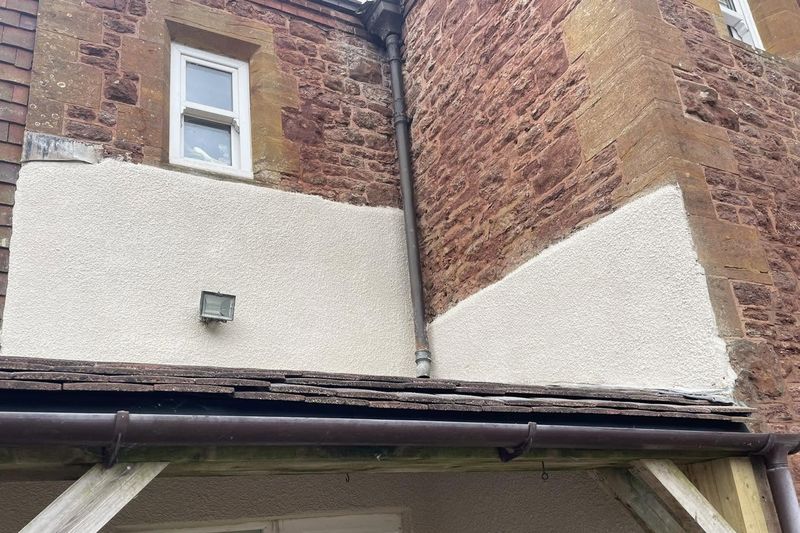 New render panels between red stone and brick on an older house, above a porch roof